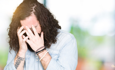 Young hipster man with long hair and beard wearing glasses with sad expression covering face with hands while crying. Depression concept.