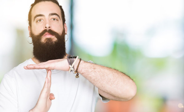 Young hipster man with long hair and beard wearing casual white t-shirt Doing time out gesture with hands, frustrated and serious face