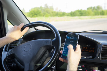 A man dials a phone number on touch screen of smartphone while driving a car