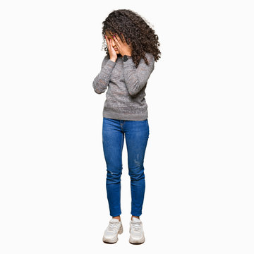 Young beautiful woman with curly hair wearing grey sweater with sad expression covering face with hands while crying. Depression concept.