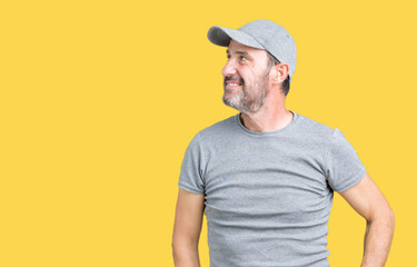 Handsome middle age hoary senior man wearing sport cap over isolated background looking away to side with smile on face, natural expression. Laughing confident.