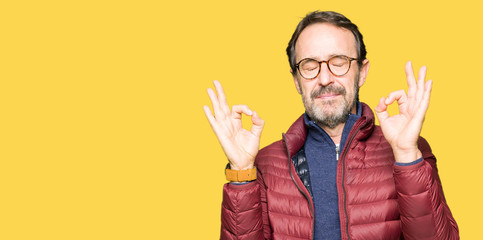 Middle age handsome man wearing glasses and winter coat relax and smiling with eyes closed doing meditation gesture with fingers. Yoga concept.