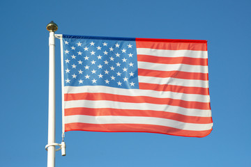 Obraz premium USA flag flapping against blue sky without clouds. American flag waving in the wind on flagpole on sunny day. Patriotic symbol of the United States of America.