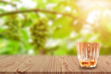 A glass of Whiskey on wooden table and light blurred nature background.
