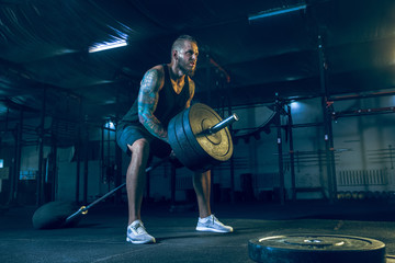 Young healthy man athlete doing exercise with the barbell in the gym. Single male model training hard and practicing in lunges. Concept of healthy lifestyle, sport, fitness, bodybuilding, crossfit.