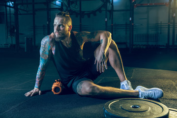 Young healthy man athlete doing exercise with the roller in the gym. Single male model training...