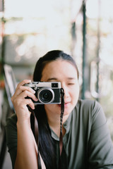 Young woman with camera.Trendy blogger use the camera in coffee shop.happy asian woman photographer holding retro fil.