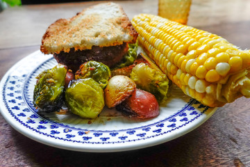 Cornwall, Connectcut, USA A plate of grilled potatoes and brussel sprouts with corn on the cob and an Impossible vegetarian burger.