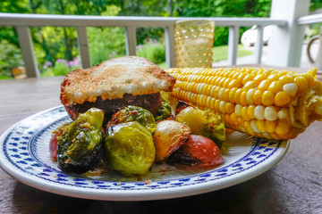 Cornwall, Connectcut, USA A plate of grilled potatoes and brussel sprouts with corn on the cob and an Impossible vegetarian burger.