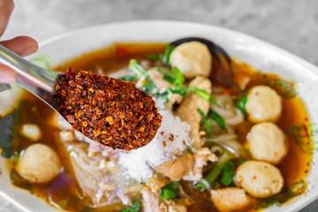 Asian woman hand pouring chili powder on noodle bowl , unhealthy eating spicy food concept background 