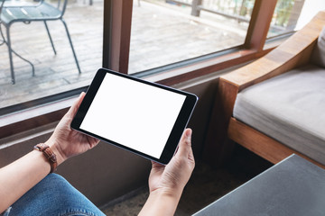 Mockup image of a woman holding black tablet pc with blank white screen while sitting in cafe