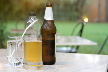 Close up of the cold glass beer with froth and bottle of beer on table in pub & restaurant background.
