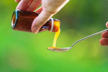 Man hand pouring medication or antipyretic syrup from bottle to spoon