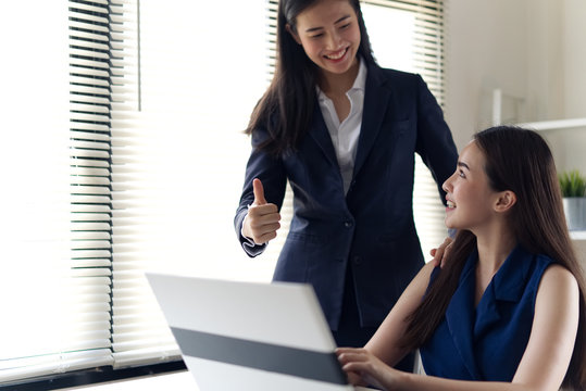 Couple Colleagues Working Together. Asian Business Woman Leader Giving Congratulation To Young Lady Girl By Thumb Up Her Finger To Her. The Girl Looking Her Boss With Smile At Office. Good Teamwork.