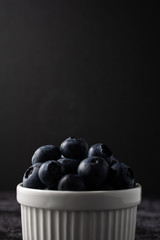 Raw blueberry in a white bowl on dark background.