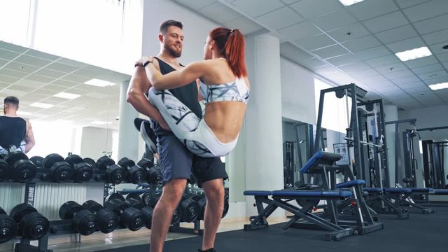 Young woman doing abs with her legs on boyfriend. Strong man holding females legs while she doing exercise. Cheerful girl lifts her body with her legs wrapped around her boyfriend.