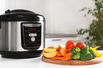 Modern multi cooker and wooden board with vegetables on white table indoors