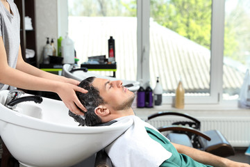Stylist washing client's hair at sink in beauty salon