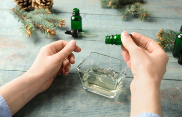 Woman pouring essential oil into bowl from bottle at table, closeup