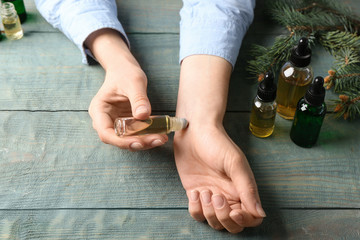 Woman applying essential oil on wrist at wooden table, closeup - obrazy, fototapety, plakaty