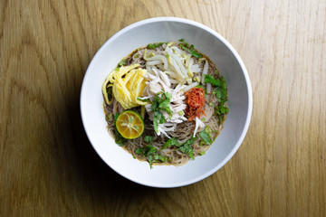 A traditional Sarawak Laksa in white bowl on wooden background.It's a spicy and flavorful noodle dish famous in Sarawak, Malaysia