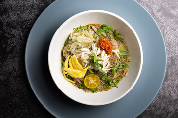 A traditional Sarawak Laksa in white bowl on dark background.It's a spicy and flavorful noodle dish famous in Sarawak, Malaysia