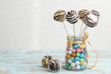 Glass jar with tasty cake pops and dragee on table against light background, space for text