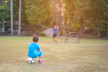 Soccer boys sitting on the ball in the football playground waiting his father teaching him.