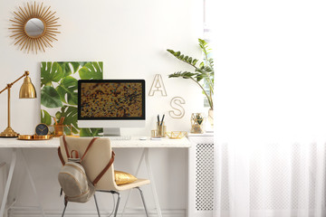 Modern workplace with computer and golden decor on desk near wall. Stylish interior design