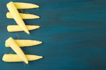 THE YOUNG CORN RAW ON A DARK TEXTURED WOODEN BACKGROUND