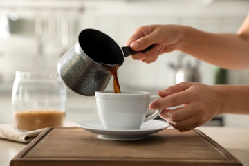 Woman pouring fresh coffee into cup at table in kitchen, closeup