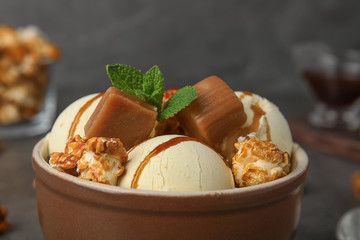 Delicious ice cream with caramel and popcorn in bowl on table, closeup