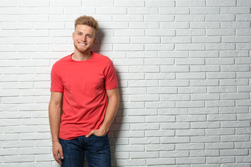 Obraz na płótnie Canvas Young man wearing blank t-shirt near white brick wall. Mockup for design