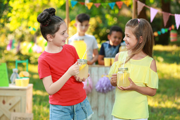 Cute little girls with natural lemonade in park. Summer refreshing drink