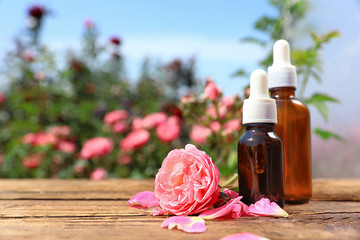 Bottles of essential oil and fresh rose on wooden table against blurred background. Space for text