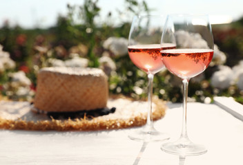 Glasses of rose wine and straw hat on white wooden table outdoors. Space for text