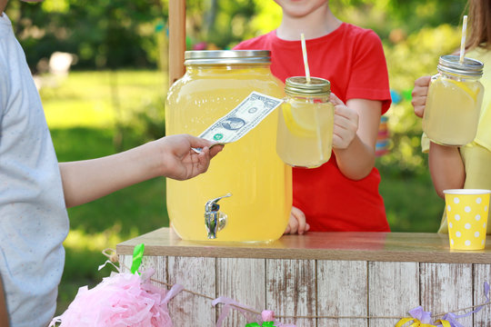 Little girls selling natural lemonade to boy in park, closeup. Summer refreshing drink