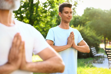 Men practicing morning yoga in sunny park