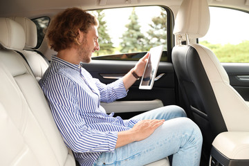 Attractive young man with tablet on backseat in luxury car