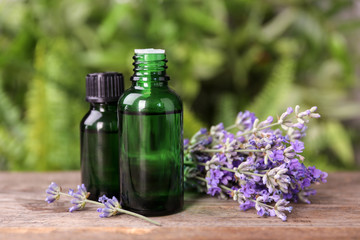 Bottles with natural lavender essential oil on wooden table against blurred background
