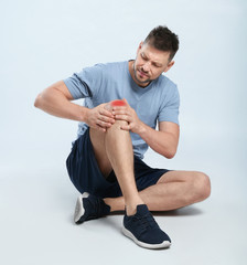 Full length portrait of man with knee problems sitting on grey background