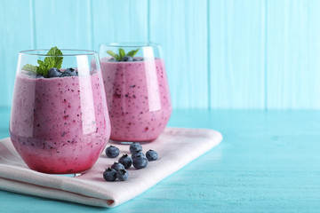Glasses of tasty blueberry smoothie and fabric on light blue wooden table, space for text