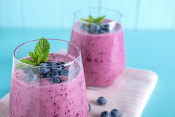 Glasses of tasty blueberry smoothie and fabric on light blue table, closeup