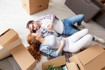 Young couple lying at the floor in empty room with unpacked boxes all arround