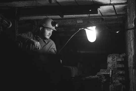 A young guy in a protective suit and helmet sits in a tunnel with a burning scrapbook. Miner in mine