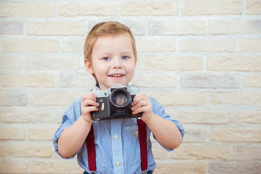 Cute little boy standing with retro camera on brick wall background