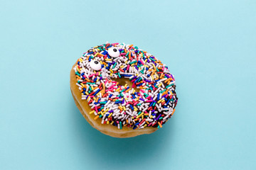 Funny shock face chocolate donut with sprinkles on a blue background, creative minimal food...