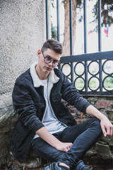 a young rebel in a jacket and jeans on the background of an old crumbling building with glasses and...