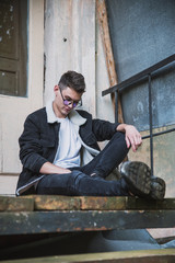 a young rebel in a jacket and jeans on the background of an old crumbling building with glasses and...