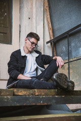 a young rebel in a jacket and jeans on the background of an old crumbling building with glasses and...